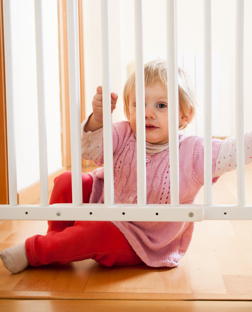 a little girl holding on a safety gate