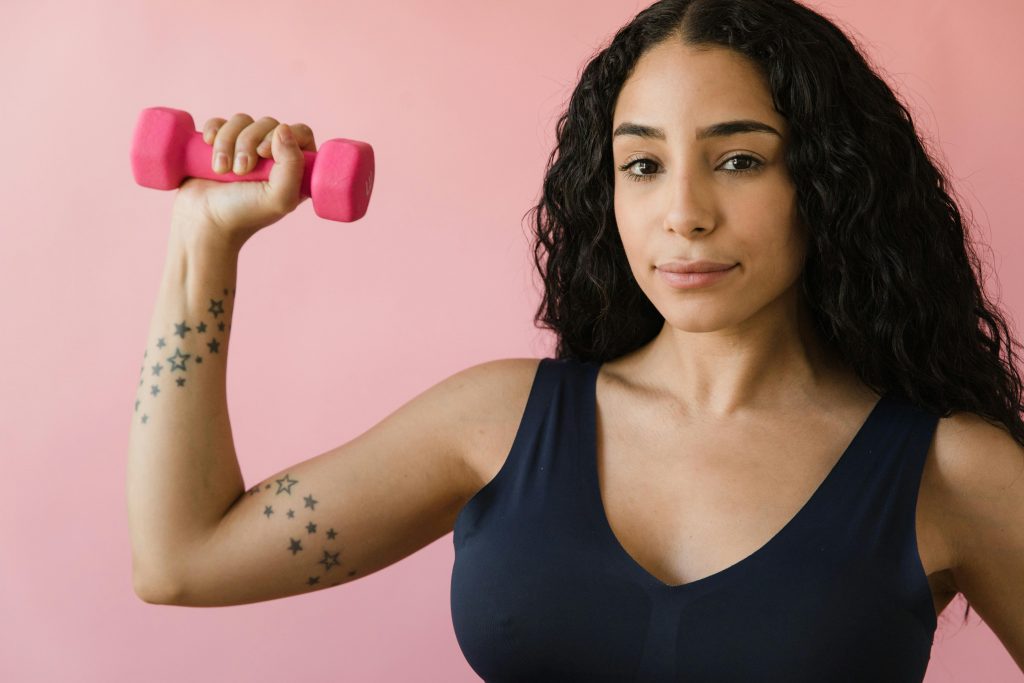 woman in athletic wear holding a pink dumbbell