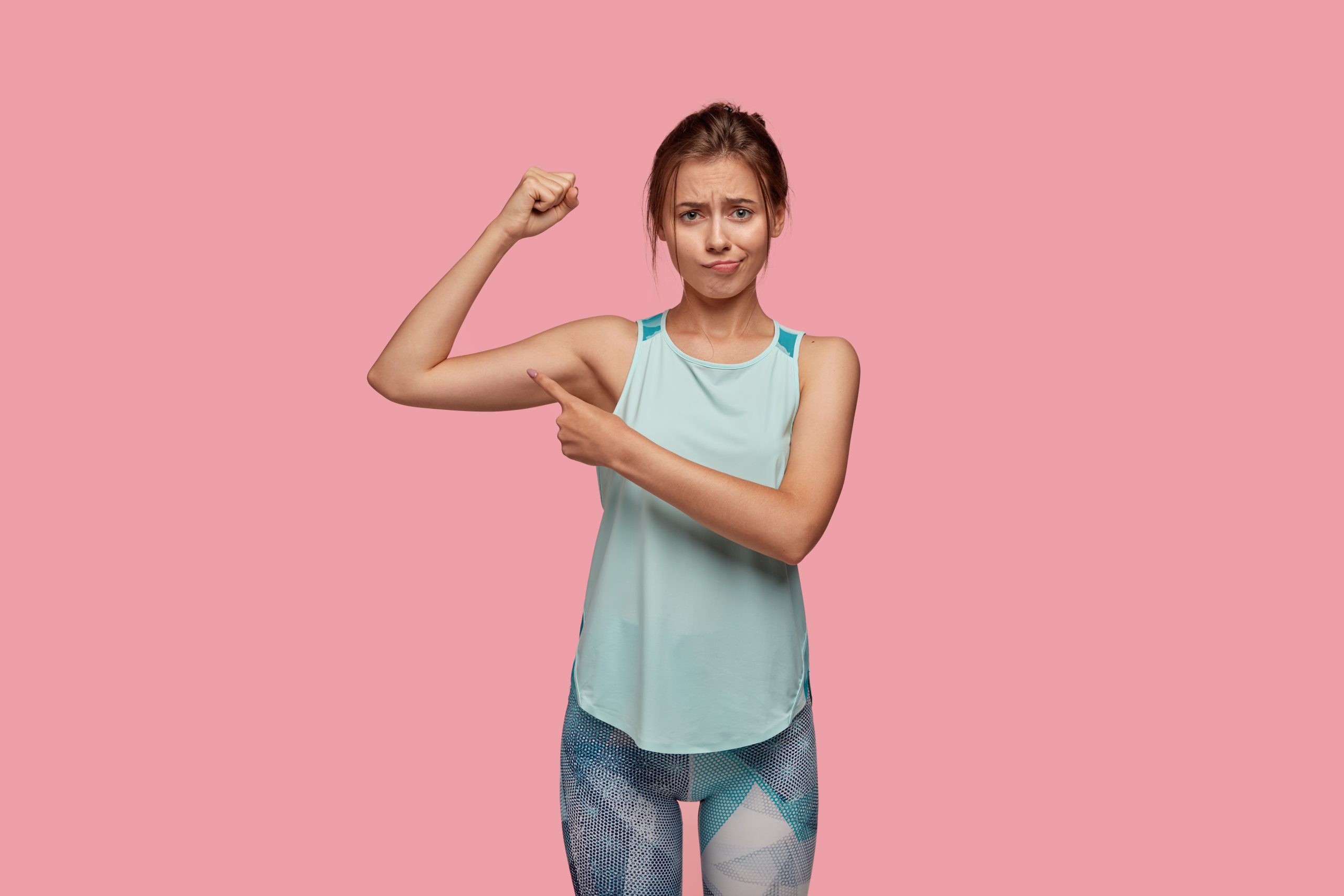 woman in athletic clothing frowning while pointing at her arm