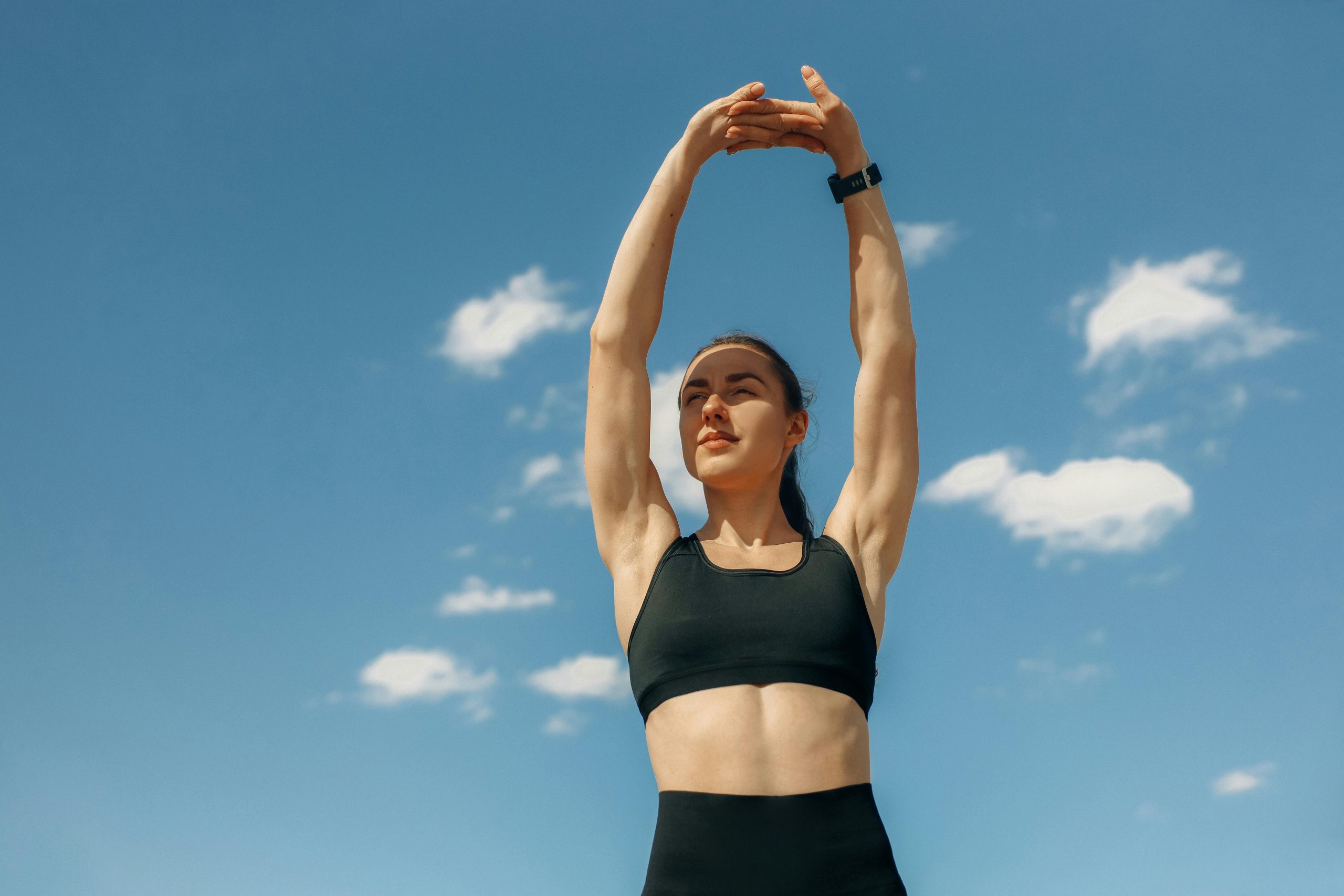 woman in fitness clothes stretching both arms upward under clear skies