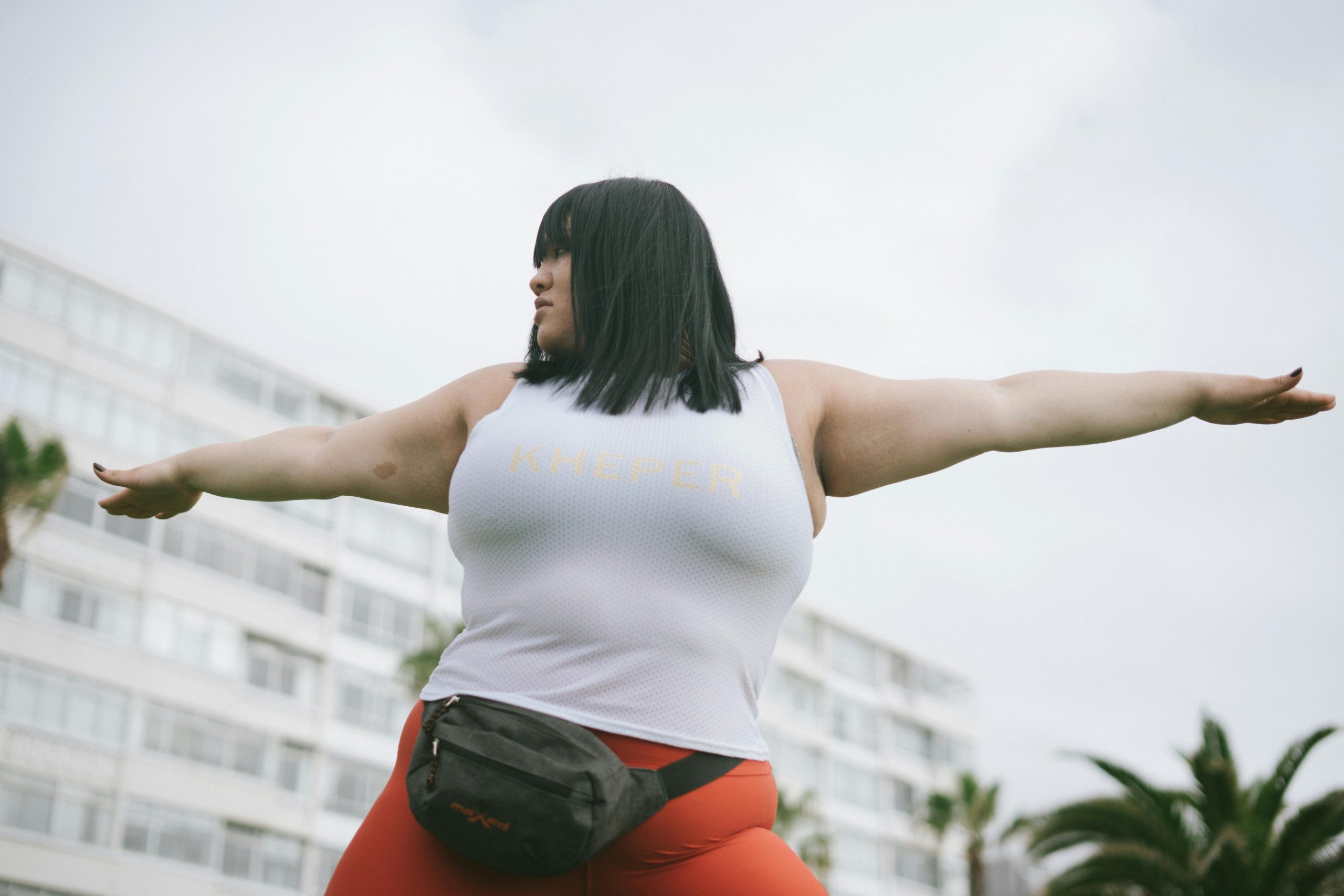 plus-size woman practicing yoga outdoors with both arms stretched out